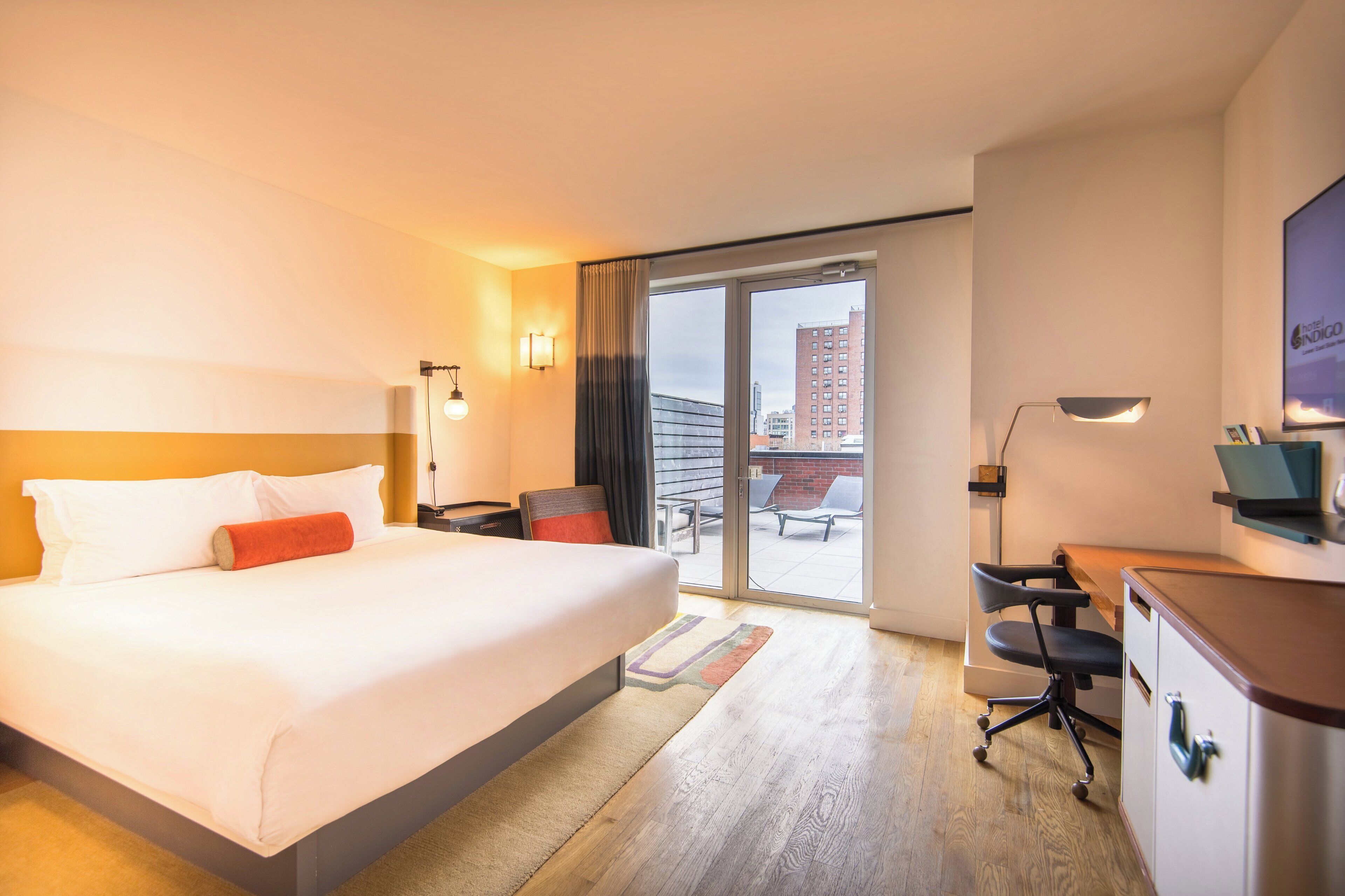 Habitació d'hotel amb un llit gran, una taula de treball, una cadira i vista a la ciutat per la finestra.