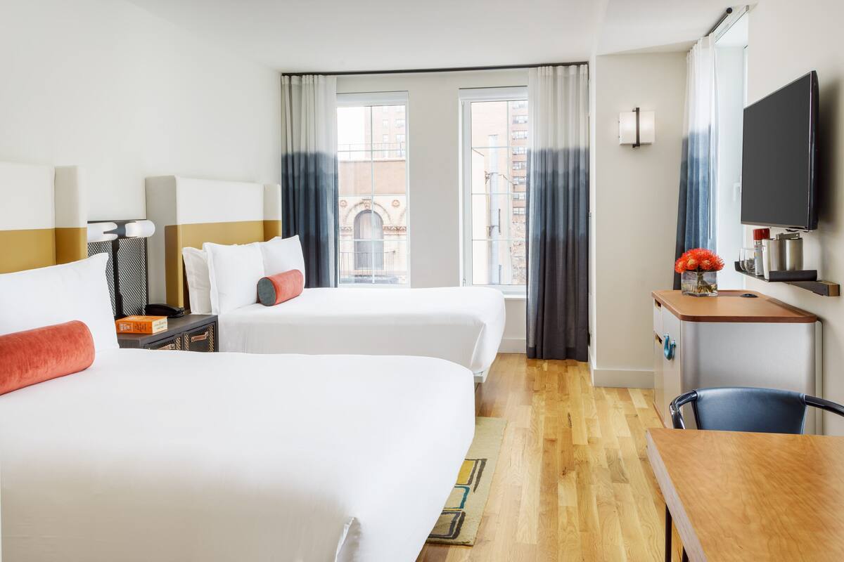 A hotel room with two beds, a desk, a TV, and a view of the city.