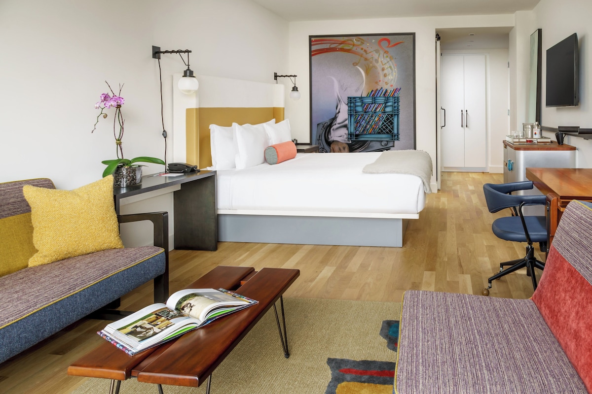Una habitación de hotel moderna con cama, escritorio, sofá, mesa de centro y televisor.