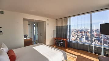 Habitación de hotel con una cama grande, un escritorio y vistas a la ciudad a través de amplios ventanales.