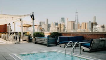 Uma área de piscina no terraço com assentos e vista para o horizonte urbano.