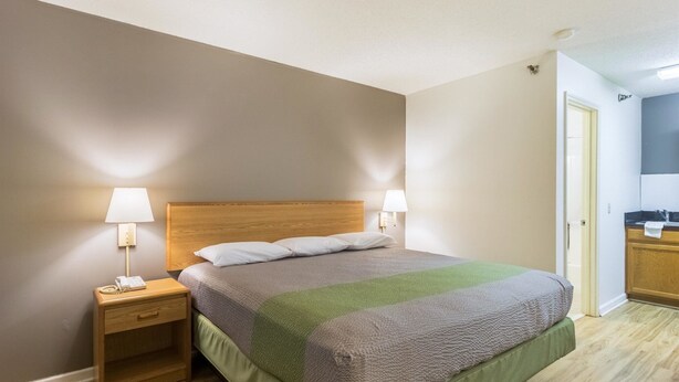 Ein ordentlich eingerichtetes Hotelzimmer mit einem Bett mit Holzkopfseitenverkleidung, zwei Nachttischlampen, einem Nachttisch mit Telefon und einer sichtbaren Badezimmertür.
