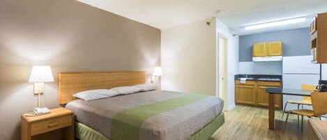 A compact hotel room with a bed, bedside tables, a small desk, and a kitchenette.