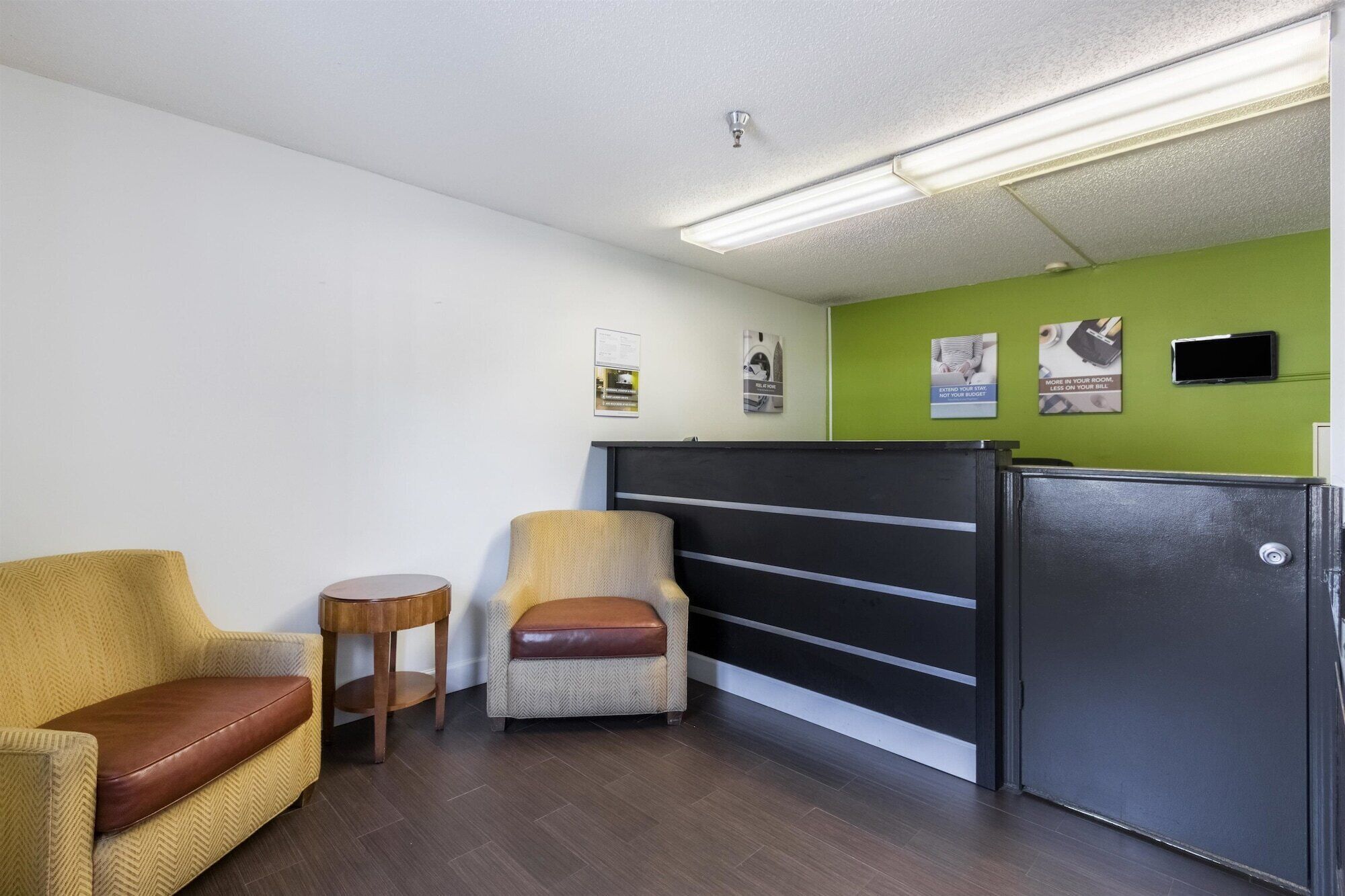 A room with a green wall, a black desk, a brown leather chair, and a wicker chair.
