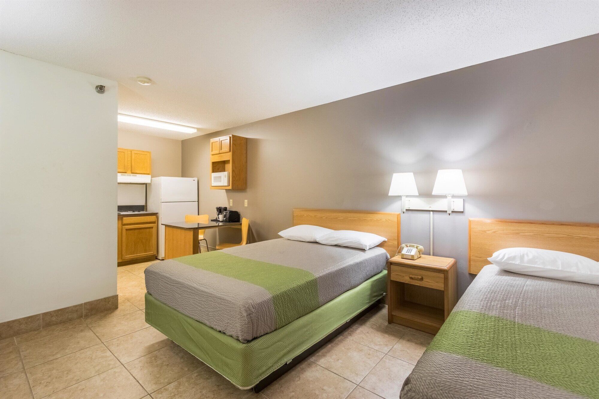 A hotel room with two beds, a kitchenette, and a small desk.