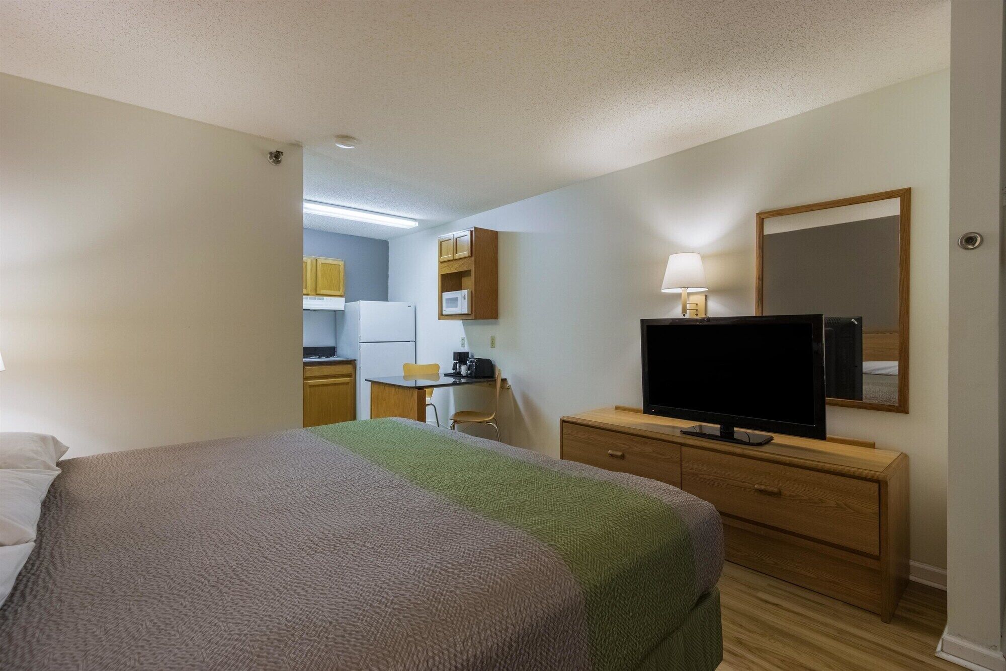 A hotel room with a bed, a television, a desk with a chair, a microwave, and a kitchenette.