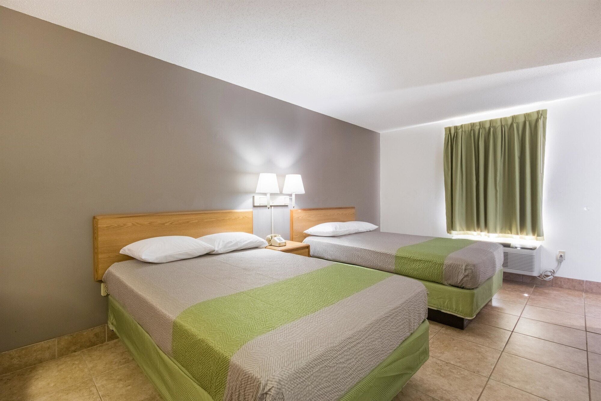 Une chambre d’hôtel avec deux lits, une table de chevet avec des lampes, une fenêtre avec des rideaux et un radiateur.