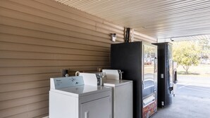 Eine Waschküche mit einer Whirlpool Waschmaschine und einem Trockner, einem Verkaufsautomaten und einem Mülleimer.