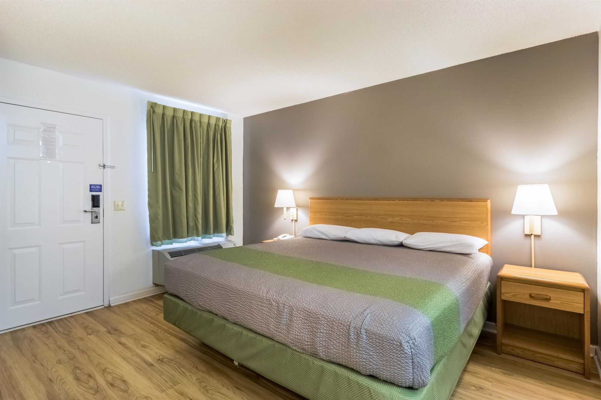 A hotel room with a bed, two bedside lamps, a nightstand, a door, and a window with curtains.