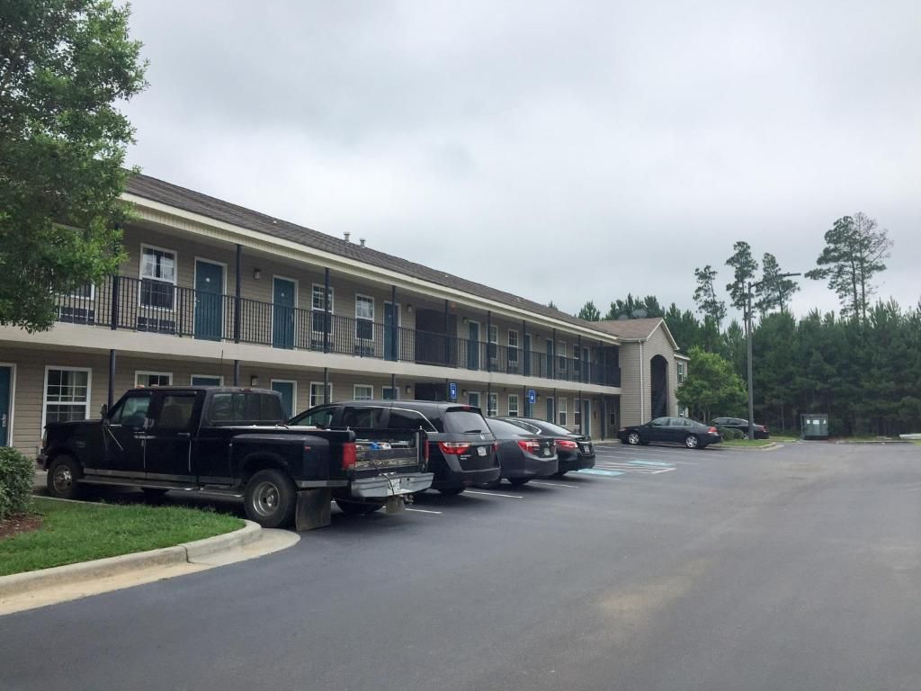 A motel with a row of parked cars and a building with a flat roof and multiple windows.