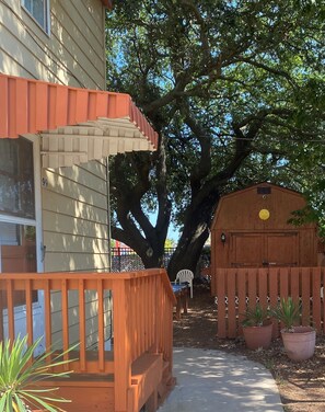 A wooden deck with a bench, a fenced area with potted plants, and a large tree providing shade. - Angie's Guest Cottage (Virginia Beach)