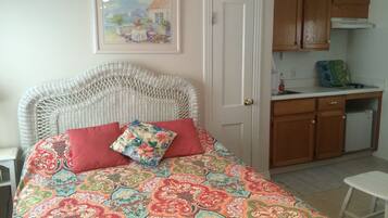 Un dormitorio con una colcha estampada, un cabecero de mimbre, un cojín rojo y un cuadro de una escena marina.
