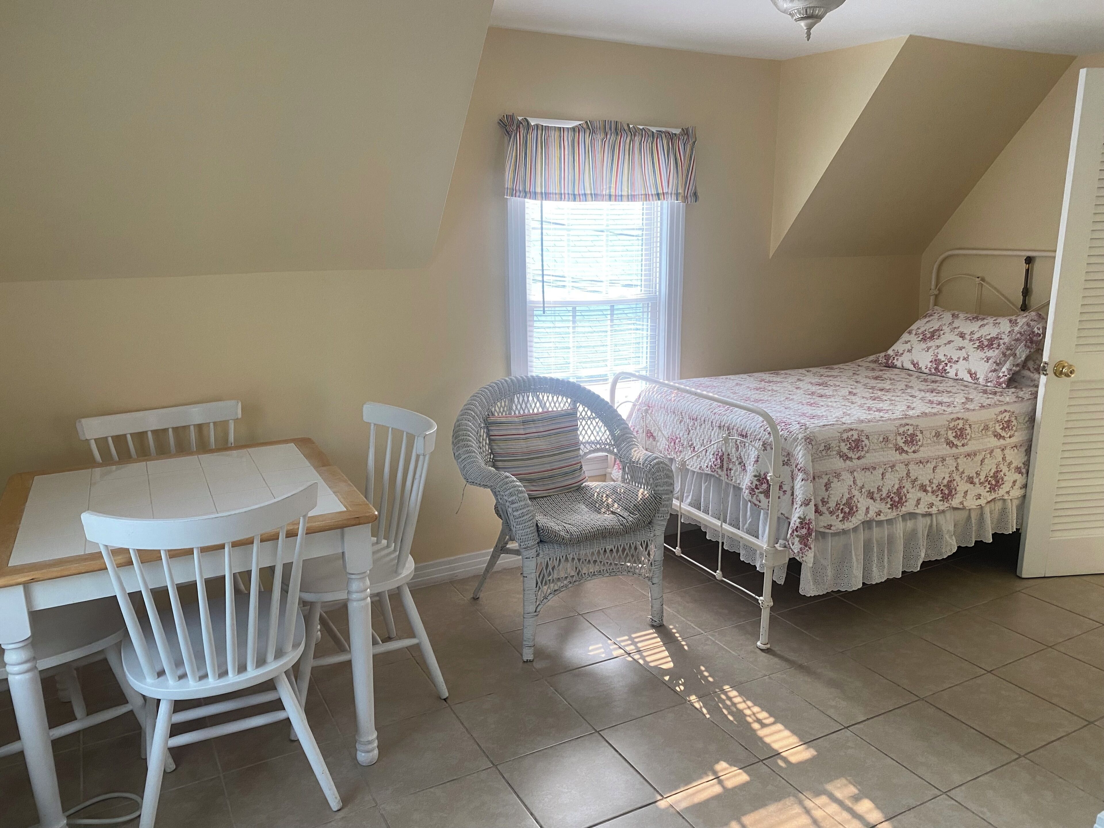 A bedroom with a bed, a chair, a table, and a window.