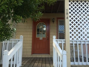 A wooden front door with a number plate, a white picket fence, and a lattice panel on the right. - Angie's Guest Cottage (Virginia Beach)