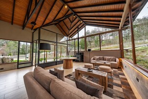Un interior moderno con techo de madera, ventanas amplias, un conjunto de sofás y una mesa de centro.