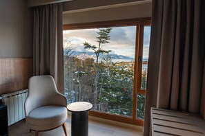 Una habitación con un ventanal grande, una silla, una mesita y un radiador.