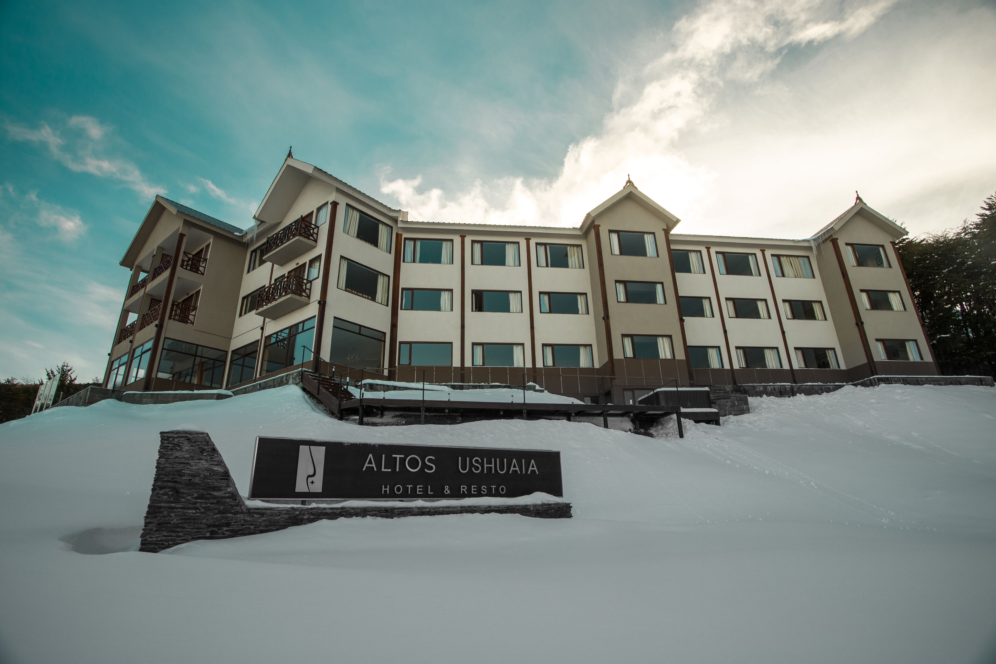 A multi-story hotel with a sign reading "Altos Ushuaia Hotel & Resto."