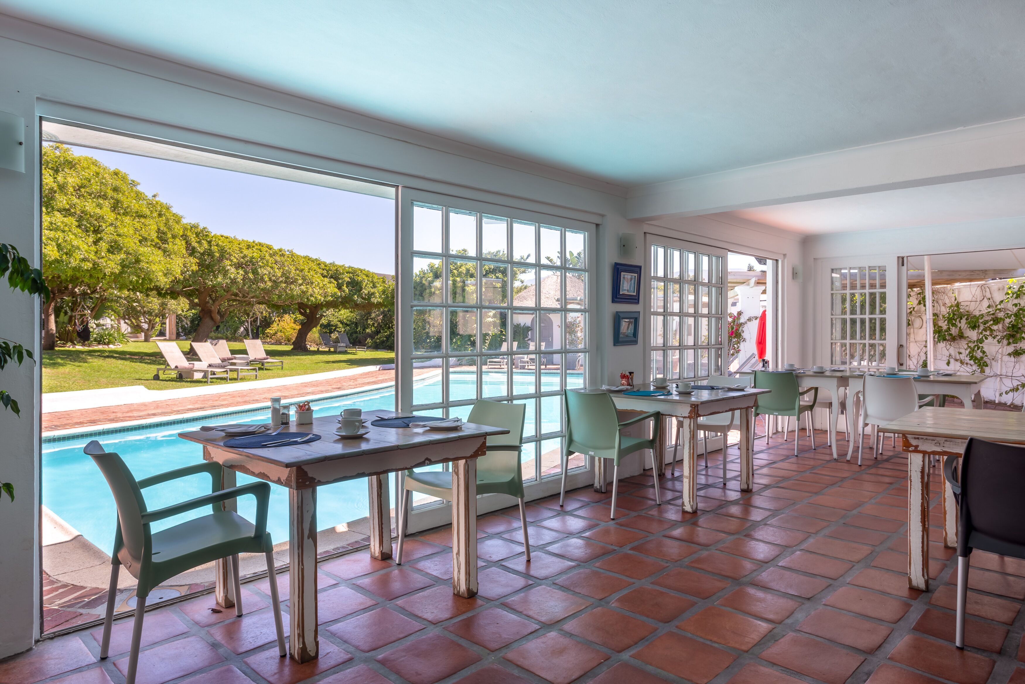 Un patio espacioso con piscina, zona de comedor al aire libre y amplias ventanas que ofrecen vista al jardín trasero.