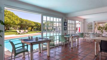 Un patio espacioso con piscina, zona de comedor al aire libre y amplias ventanas que ofrecen vista al jardín trasero.