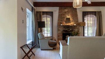 A living room with a stone fireplace, a ceiling fan, and a television.