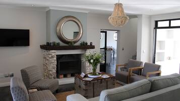 A living room with a fireplace, a mounted TV, and a chandelier.