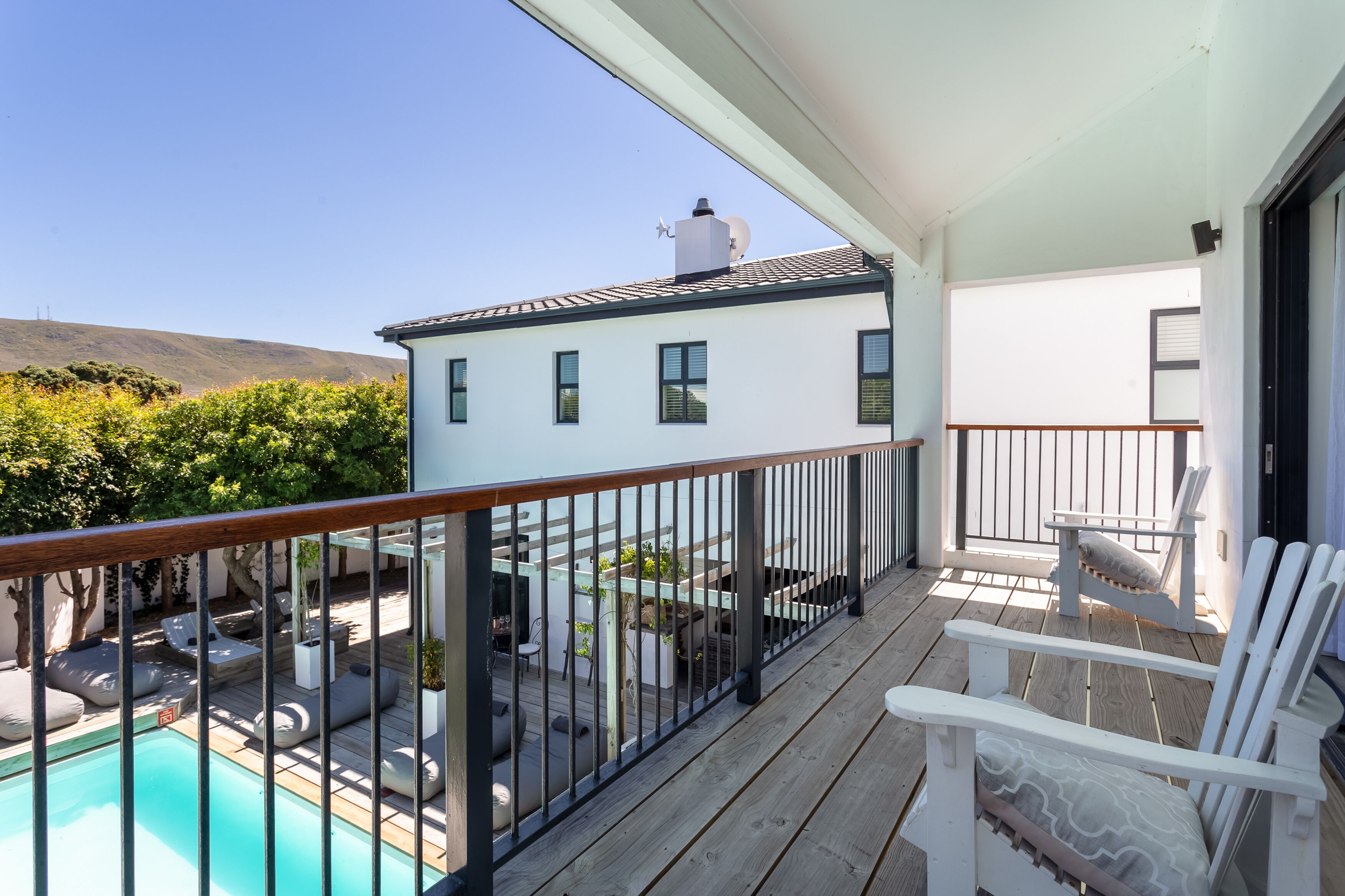 A balcony with a pool, outdoor seating, and a view of a white building with a satellite dish.