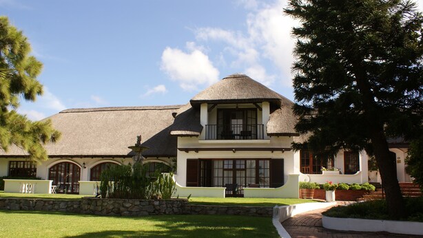 A large, two-story building with a thatched roof, stone walls, and a well-maintained lawn. - Whale Rock Luxury Lodge (Hermanus)