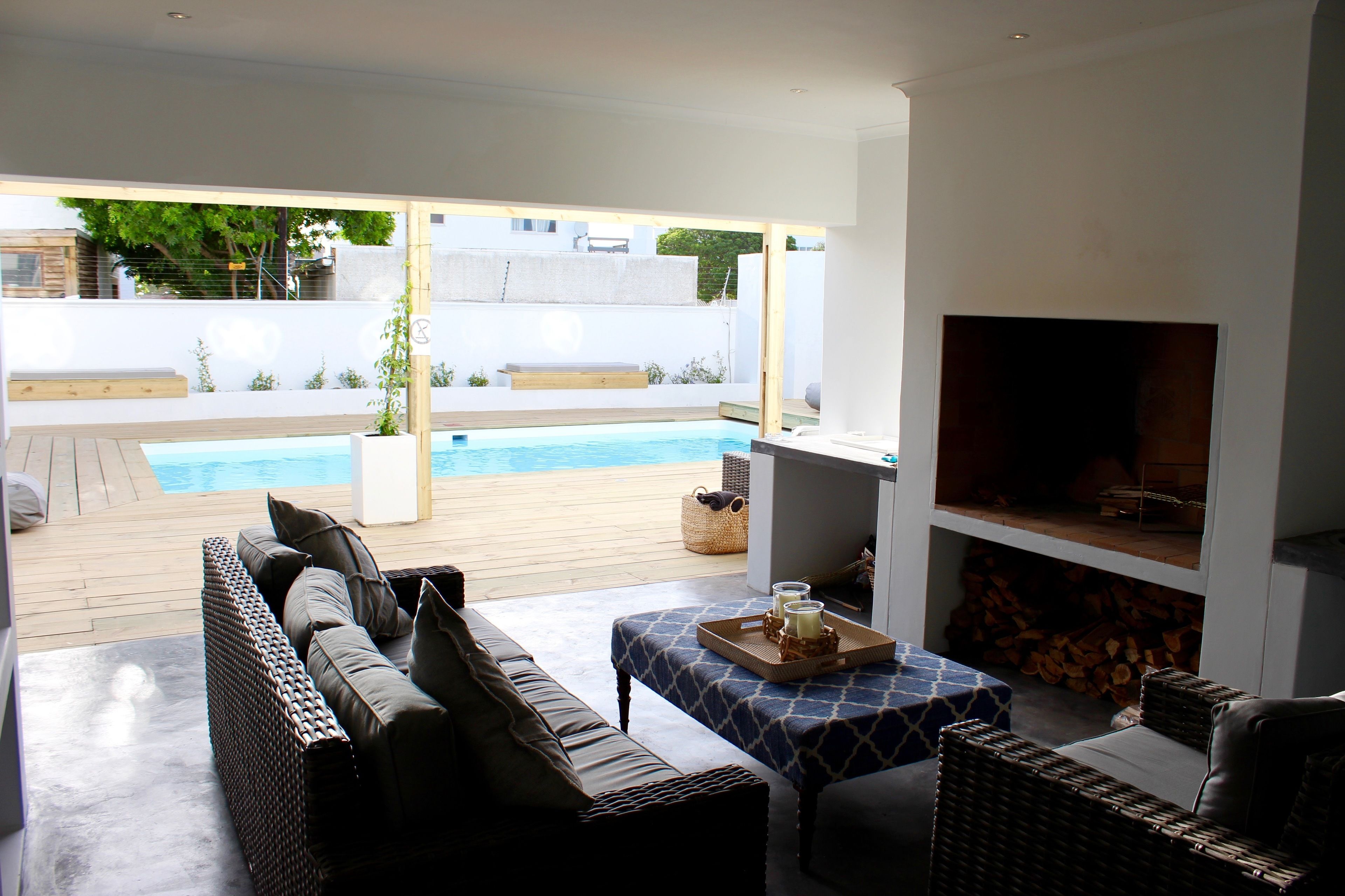 A modern outdoor living area with a pool, wicker furniture, and a fireplace.