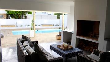 A modern outdoor living area with a pool, wicker furniture, and a fireplace.