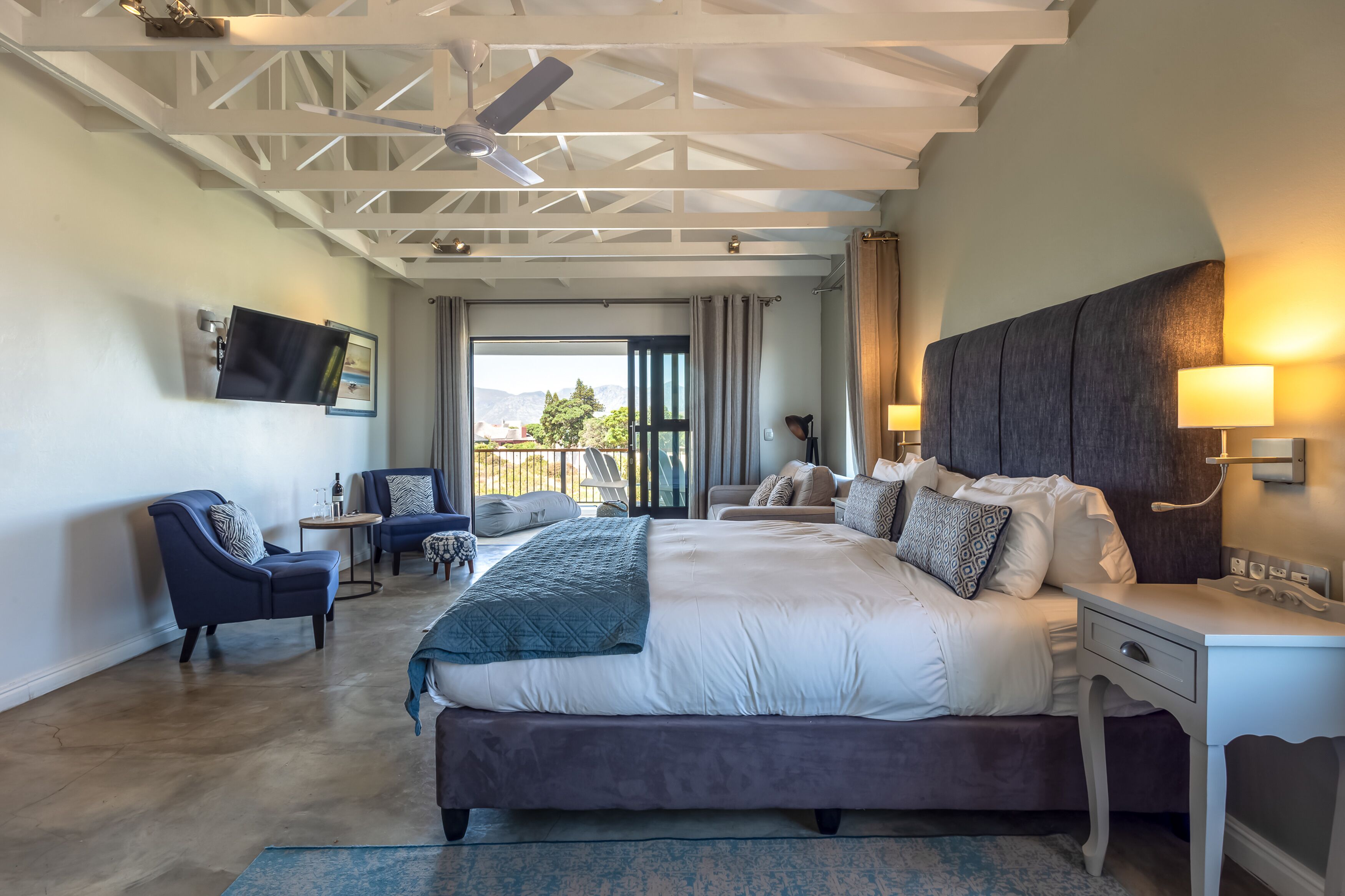 A spacious bedroom with a large bed, a desk, and a TV mounted on the wall.