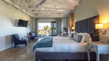 A spacious bedroom with a large bed, a desk, and a TV mounted on the wall.