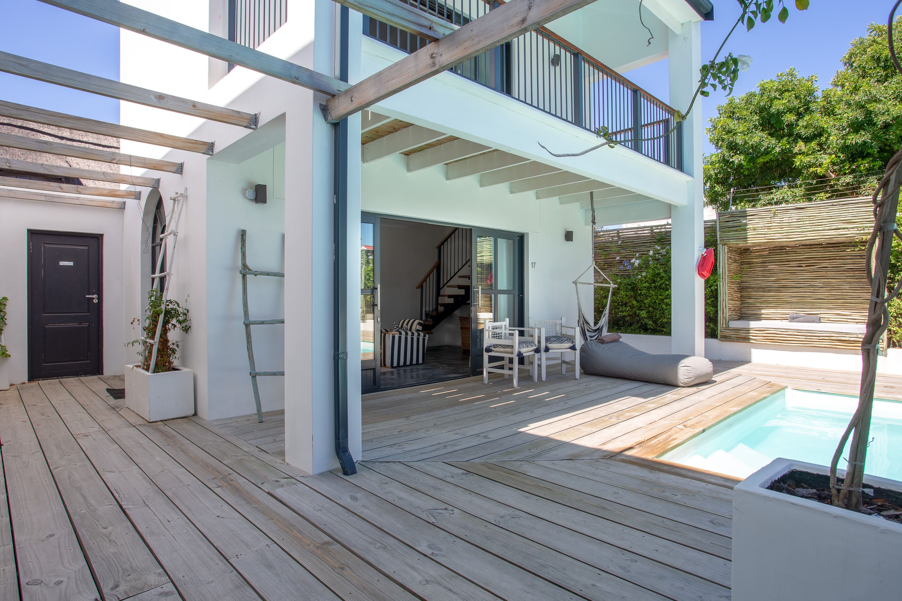 A modern house with a wooden deck, a pool, and a staircase leading to the upper floor.