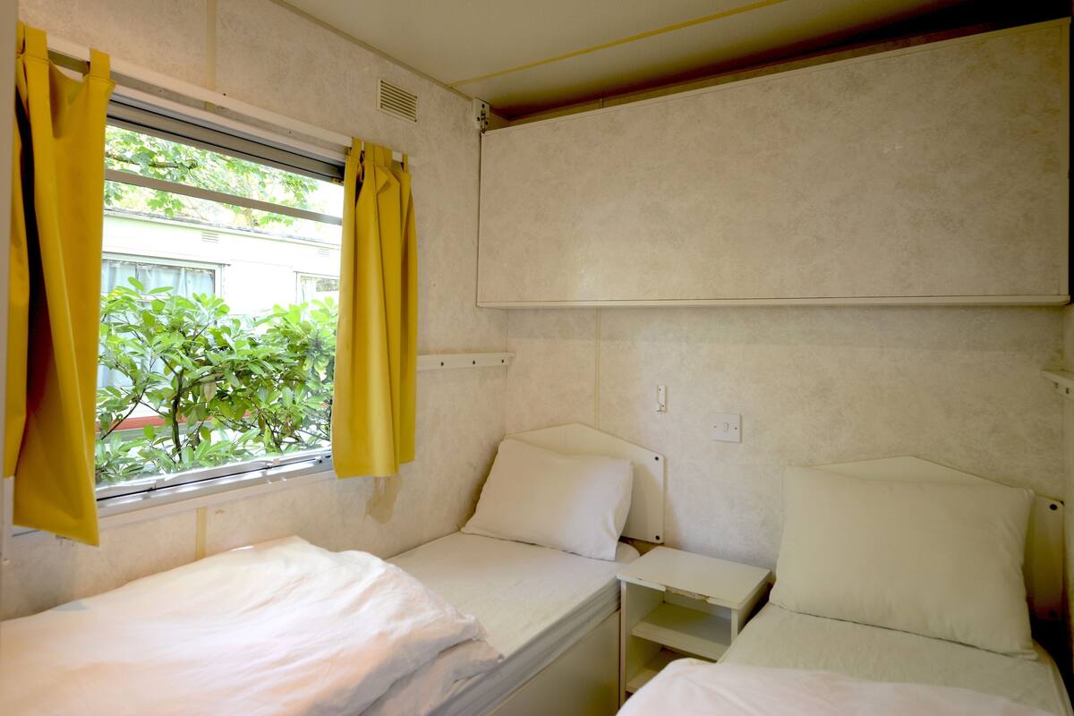 Une petite chambre avec un lit simple, une fenêtre, une table de chevet et une étagère fixée au mur.