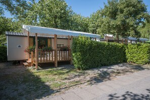 A mobile home with a covered porch, surrounded by greenery and a paved driveway. - Parco delle Piscine - Campground (Sarteano)