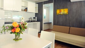 Eine moderne Küche mit weißen Schränken, einem Esstisch mit Blumenvase und einem braunen Sofa in einem Wohnbereich mit grauer Wand und einem Gemälde.