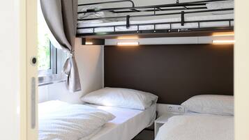 Une chambre compacte pour camping-car, dotée de deux lits superposés, d’une fenêtre avec rideaux et d’un éclairage intégré.