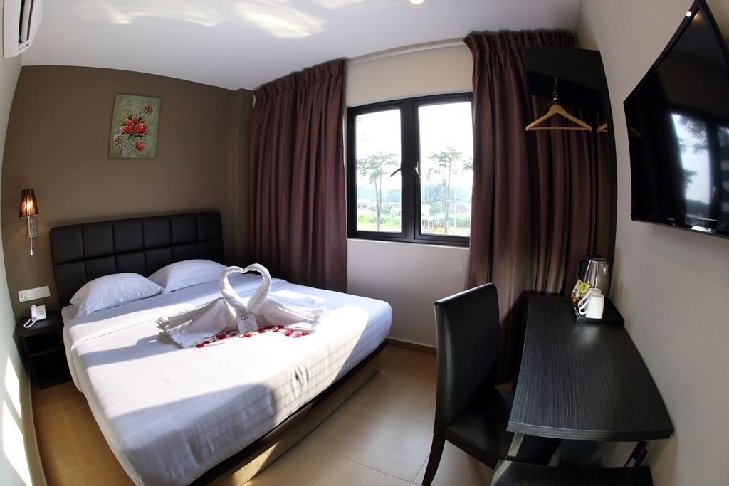 A hotel room with a bed, a desk, a chair, a TV, and a window with curtains.