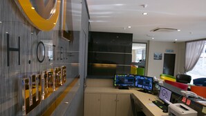 A hotel reception area with a modern design, featuring a reception desk with multiple computer monitors, a telephone, and a digital display. - GL Hotel (Kluang)