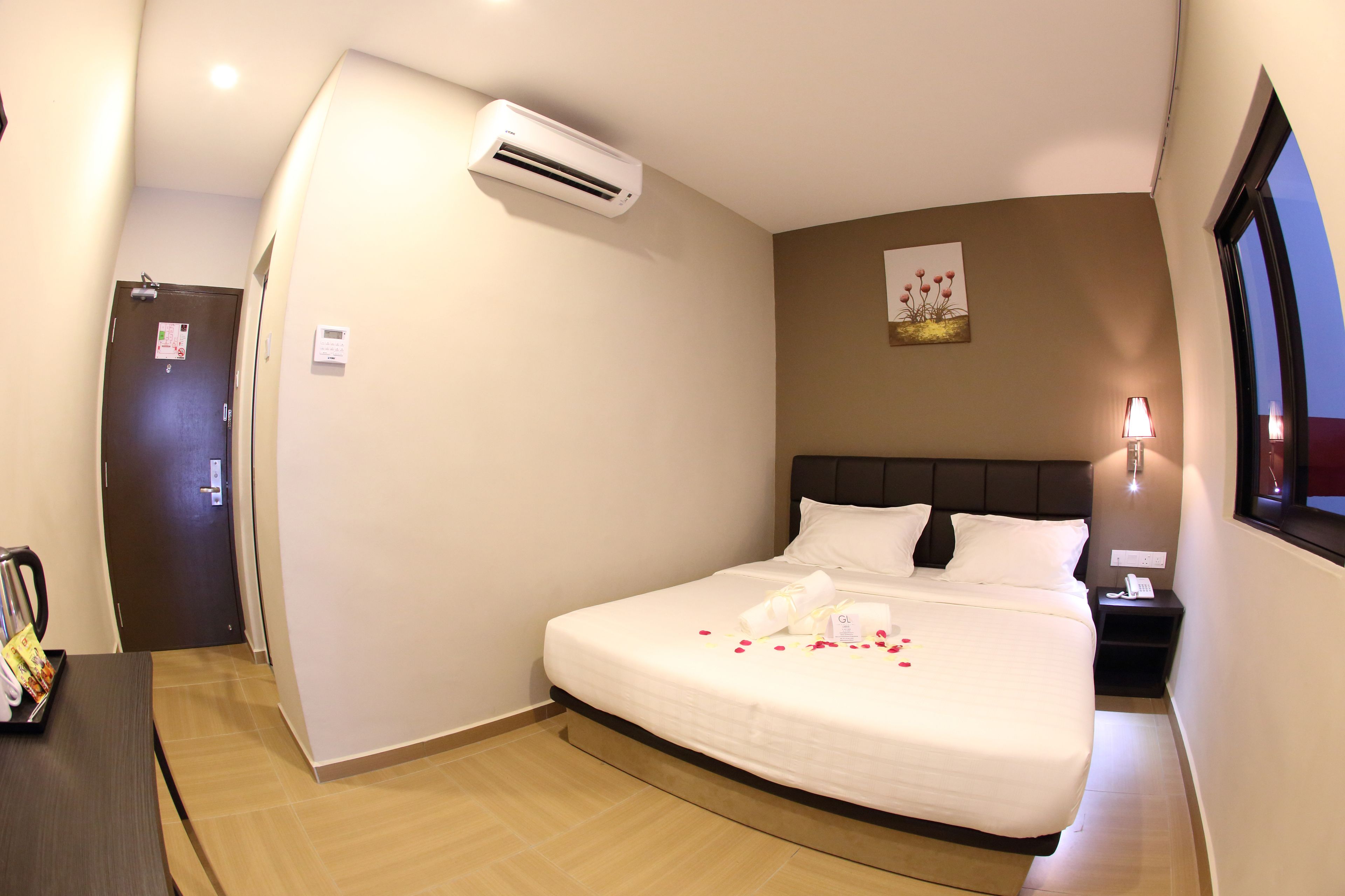 A neatly made bed with a white comforter, a bedside lamp, and a wall-mounted air conditioner.