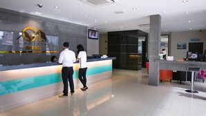 A hotel reception area with a modern design, including a reception desk, a digital screen, and a seating area with red chairs. - GL Hotel (Kluang)