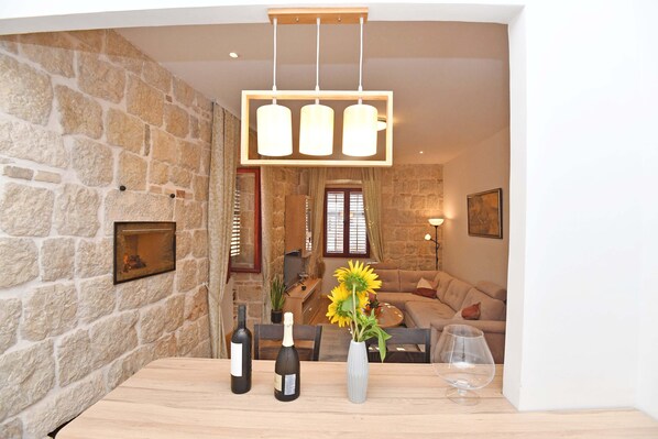 Una habitación con paredes de piedra, una mesa de madera, botellas de vino y un jarrón con girasoles.