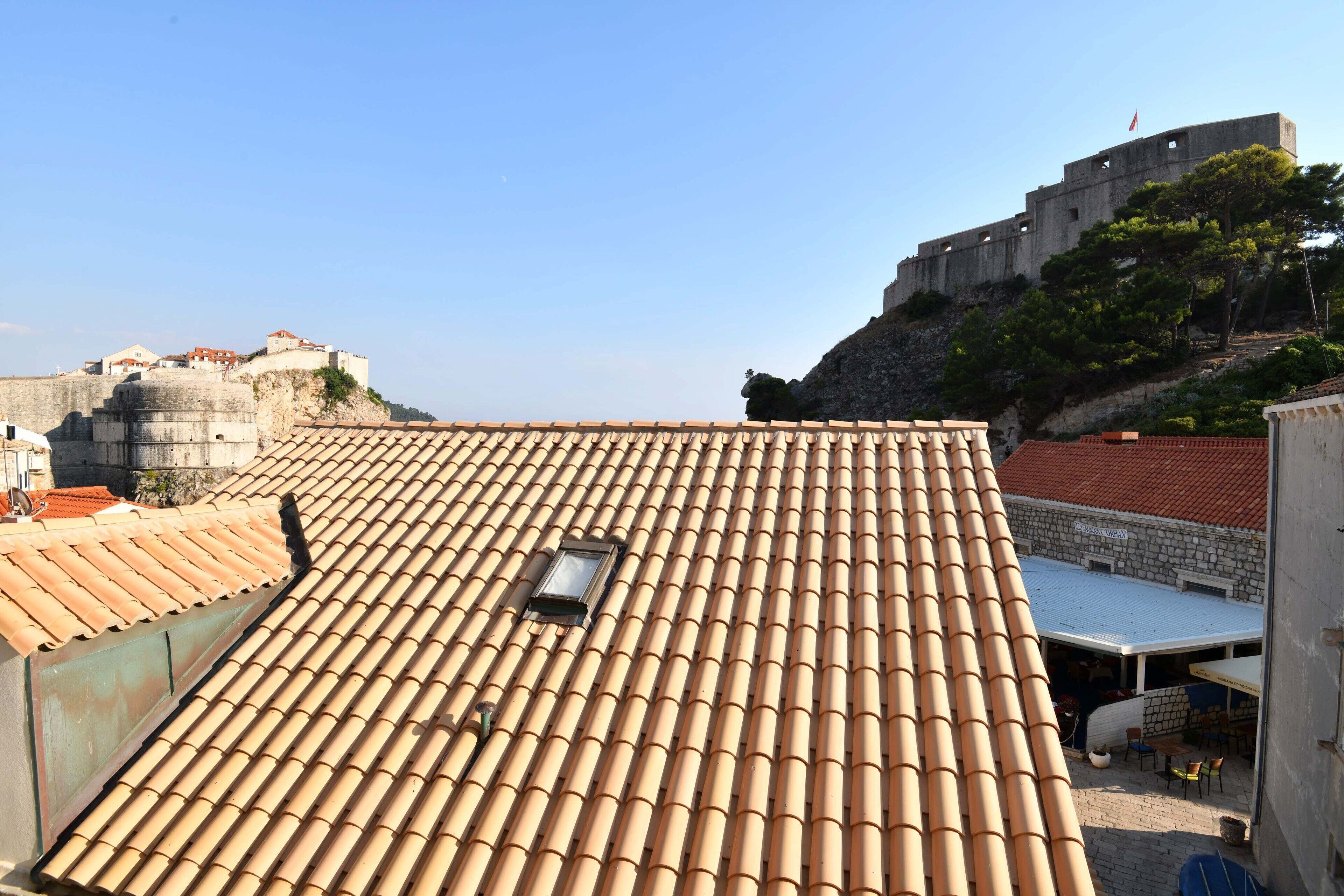 A rooftop with terracotta tiles, a small window, and a view of a historic stone building.