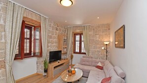 Un salon avec des murs en pierre, une table basse en bois, un canapé beige et un téléviseur posé sur un meuble en bois.