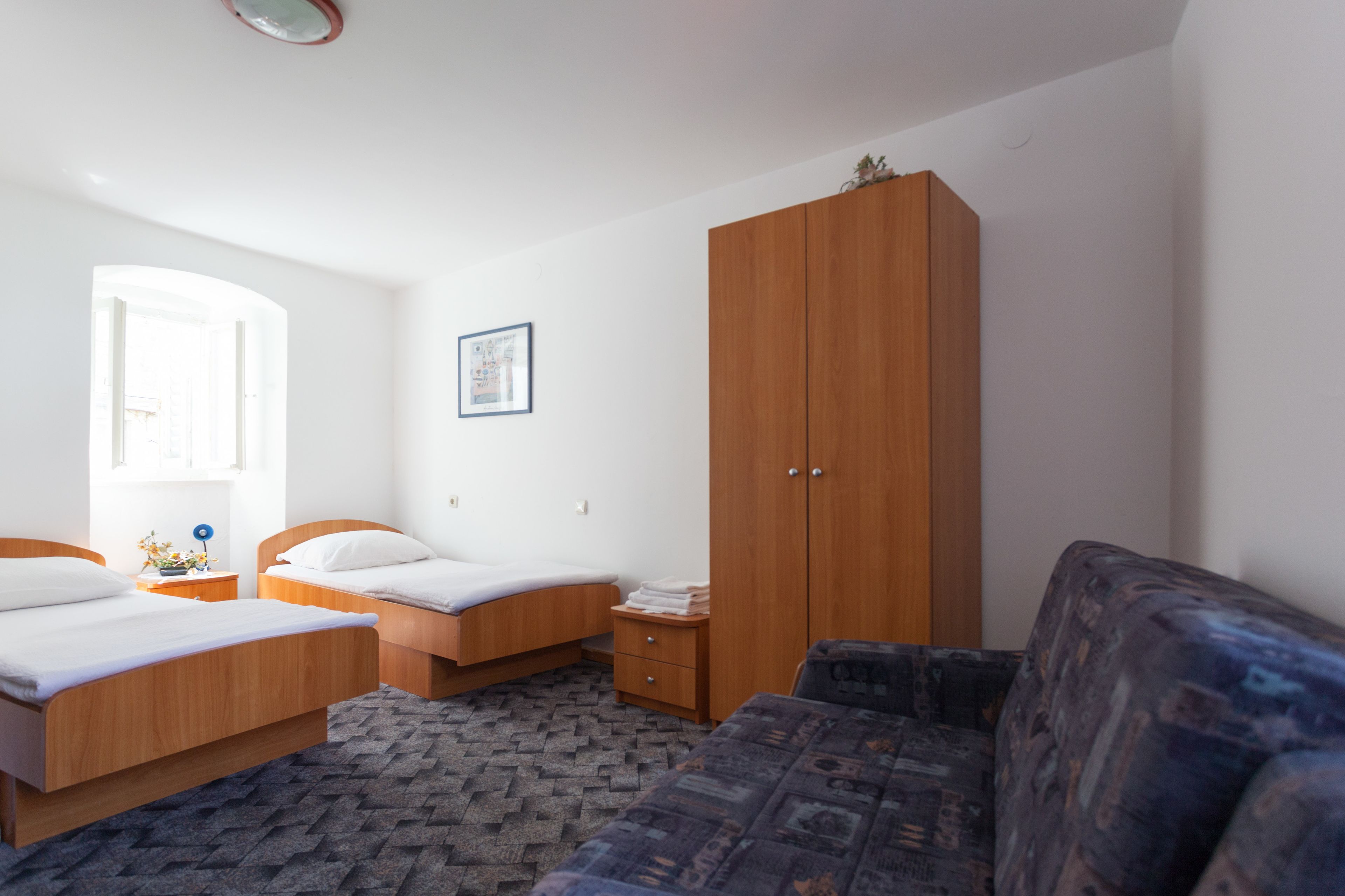 A bedroom with two beds, a wardrobe, a sofa, and a window.