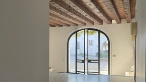 An interior space with a high ceiling, exposed wooden beams, a terrazzo floor, and a large arched doorway leading outside. - Hotel Villa Policreti (Aviano)