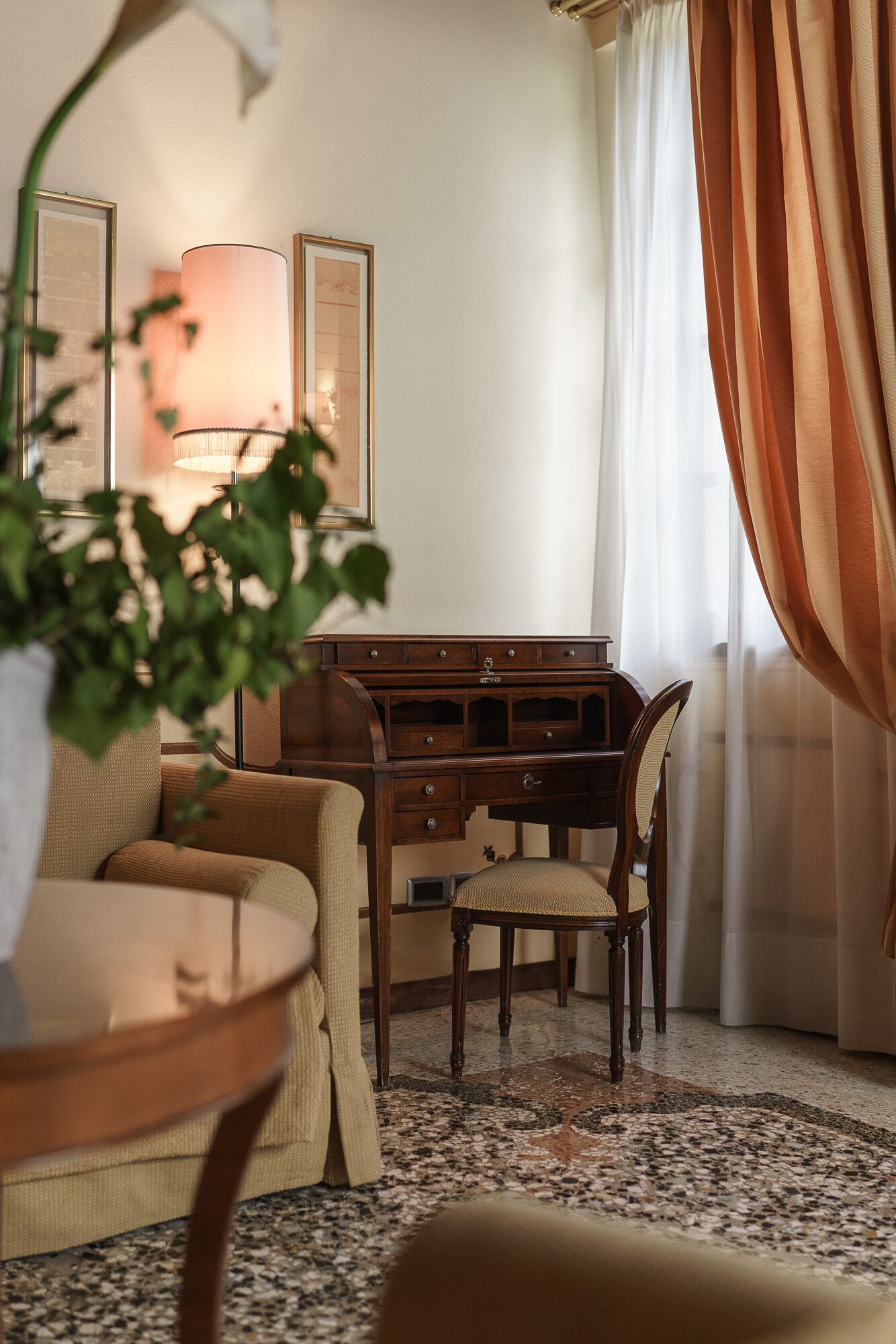 A cozy room with a wooden desk, a chair, a sofa, and a lamp.