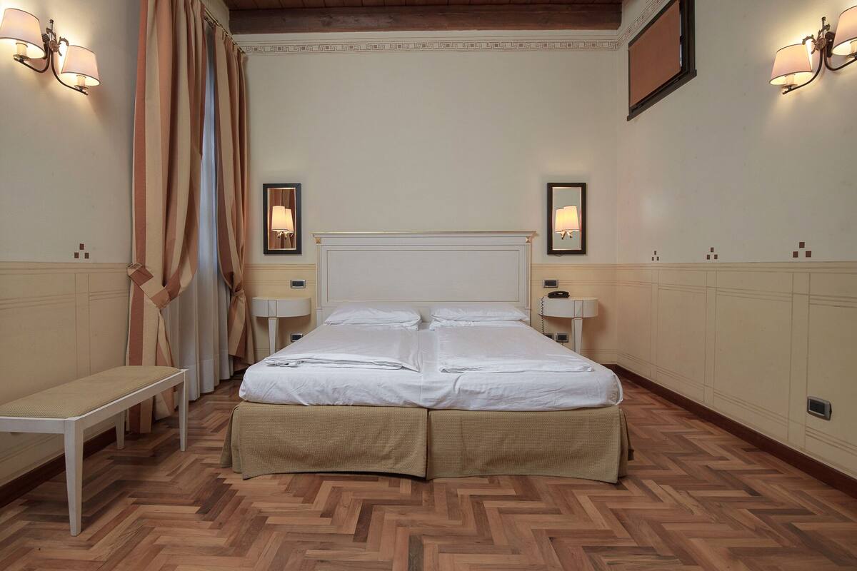 Ein Hotelzimmer mit einem großen Bett, zwei Nachttischen, einer Bank und einem Spiegel an der Wand.