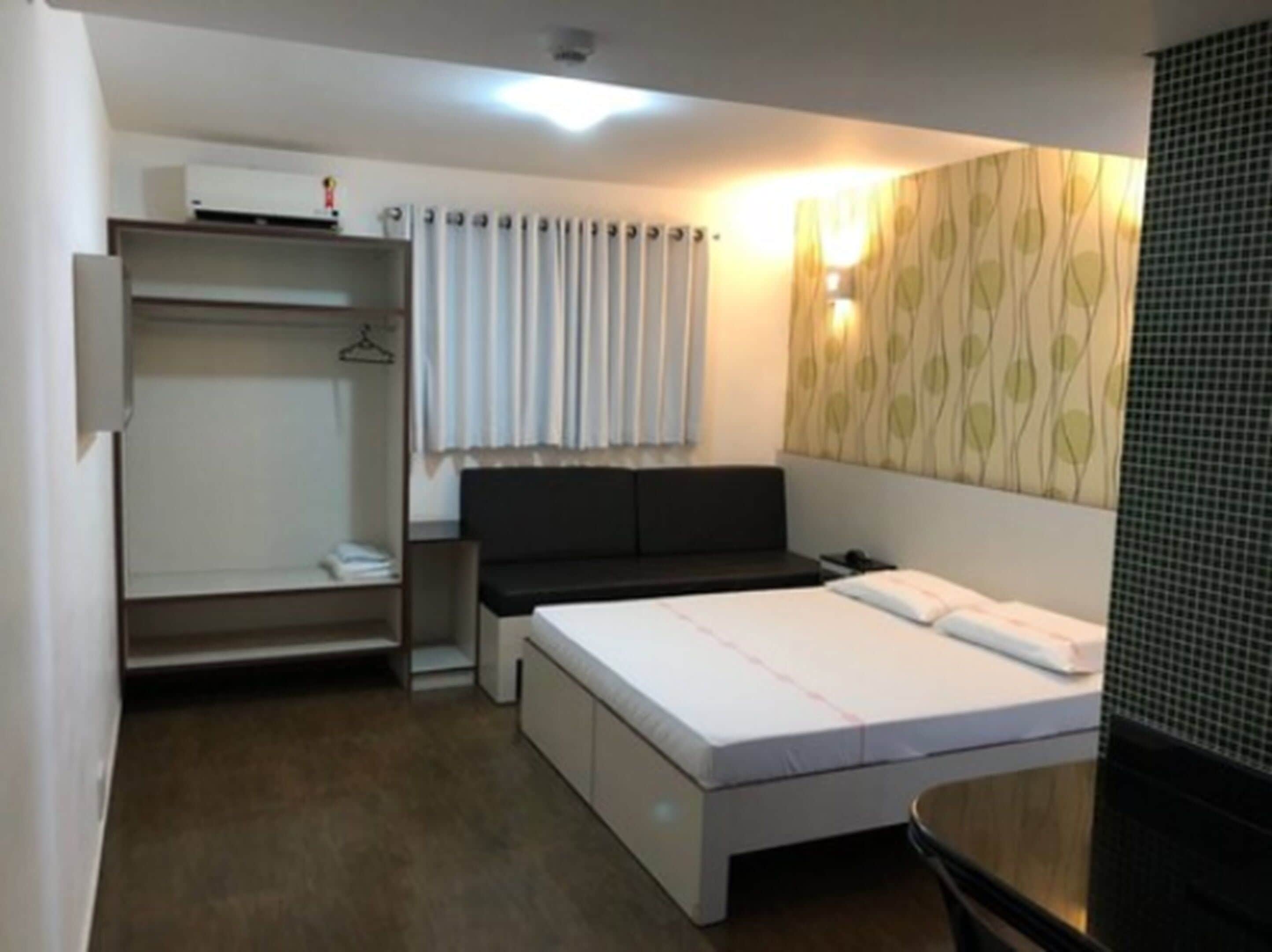 A hotel room with a bed, a desk, a wardrobe, and a window with curtains.