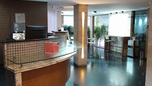 A modern reception area with a curved reception desk, a tiled wall, and a glass partition. - Hotel Calandre (São Paulo)