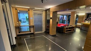 A modern hotel lobby with a shiny black tiled floor, a reception desk, and a red sofa. - Hotel Calandre (São Paulo)